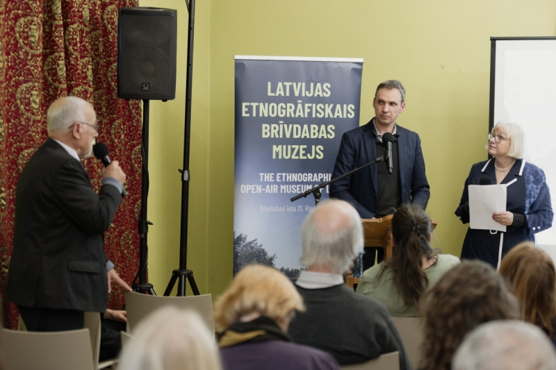 3 cilvēki stāv zālē, publikas priekšā