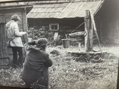 Vēsturisks foto: fotogrāfs iemūžina senu koka ūdens sūkni (pumpi) ar metāla spainīti.