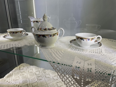 Izstādes vitrīna ar tamborētām sedziņām un porcelāna servīzi. 