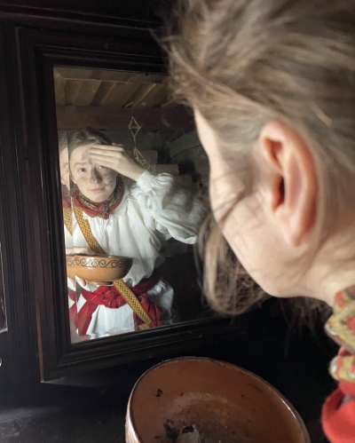 Meitene pie spoguļa tradicionālā veidā krāso seju ar oglēm.