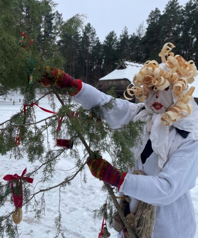 Meteņu maska Ķekata: sieviete baltā kreklā ar ēveļskaidu matiem un kadiķa zaru.