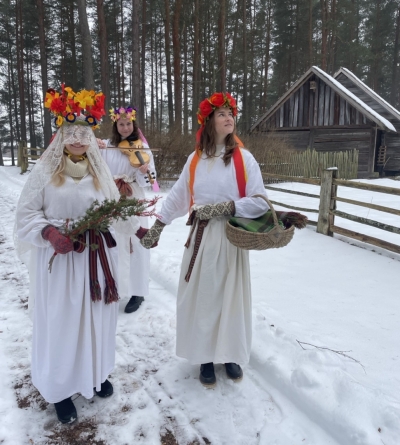 Trīs meitenes sniegotā ainavā, tērpušās kā līgavas, ar ziediem un vijoli.