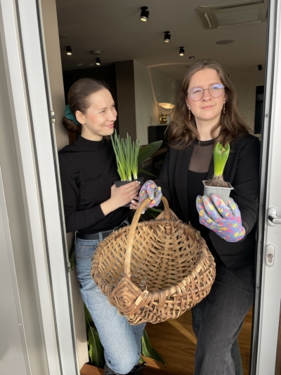 Divas meitenes modernā interjerā ar senu grozu un augu stādiem.