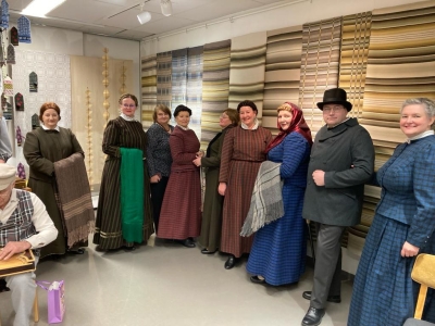 Studijas dalībnieki telpā pie krāsainiem, austiem audekliem