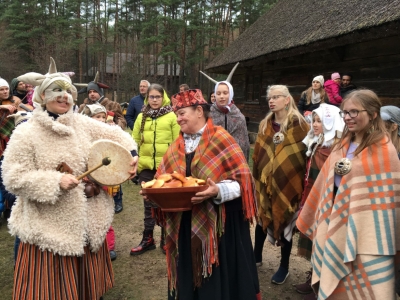 Mārtiņdienas maskas un Kurzemes sētas saimniece ar pīrāgu bļodu.