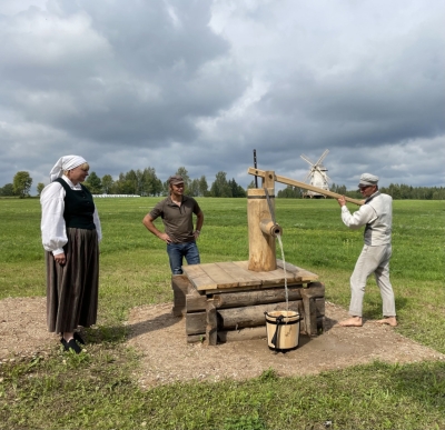 Trīs cilvēki pumpē ūdeni no akas
