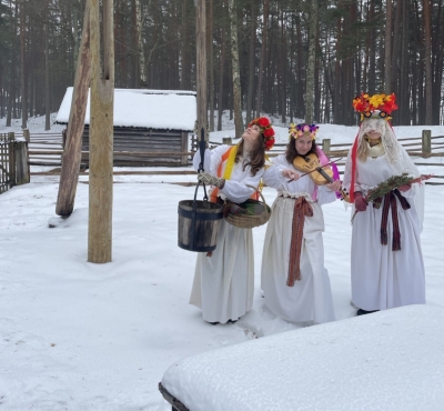 Baltos tērpos un puķu vainagos pie akas sniegā.