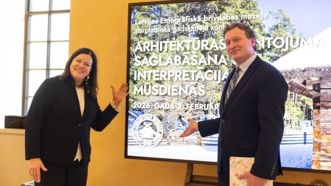 Muzeja direktore un direktora vietnieks stāv pie prezentācijas ekrāna konferencē par arhitektūras mantojumu. 