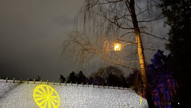 Kurzemes laidars tumsā ar dzeltena rata (saules simbola) gaismas projekciju uz sienas. 