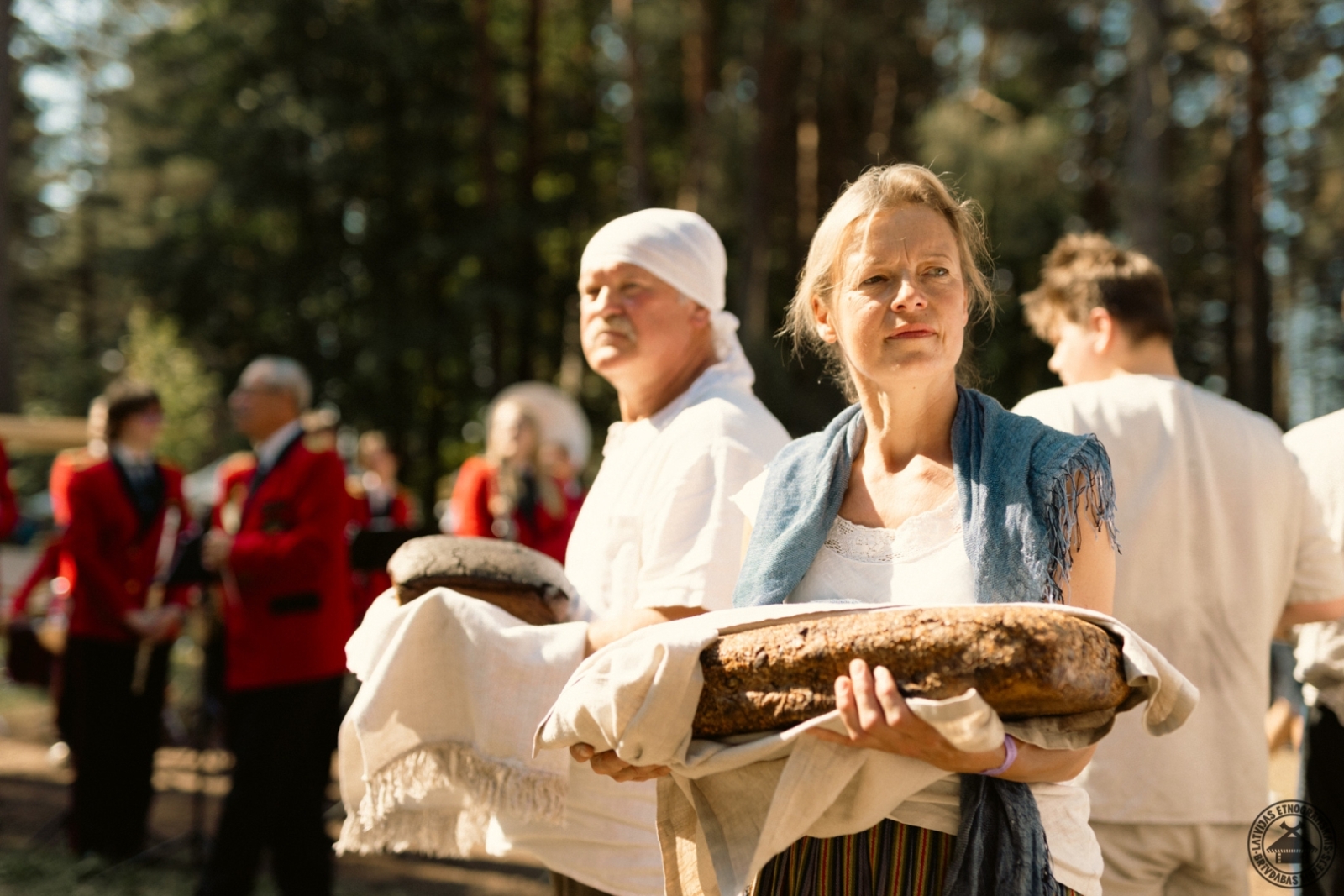Maizes cepēju grupa aplī ar mugurām viens pret otru; katram rokās liels, spēcīgs rudzu maizes kukulis. 