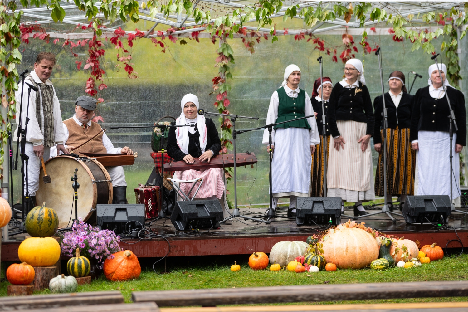 Folkloras kopa uzstājas uz skatuves, kas rotāta ar ķirbjiem un rudens vītnēm