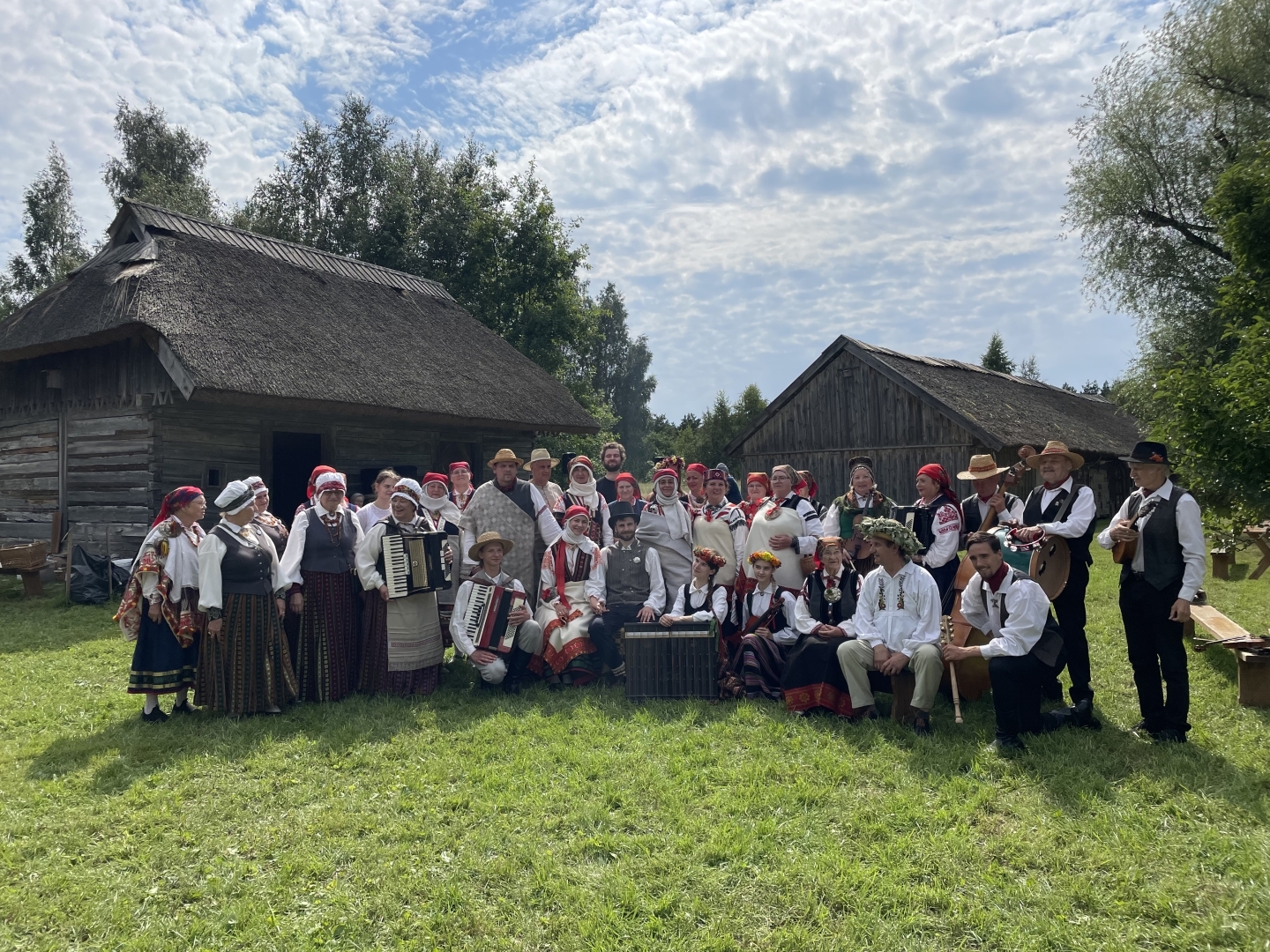 Kuplais kāzu viesu pulks tautastērpos un svētku drēbēs sanācis kopbildei Vītolnieku zaļajā pagalmā.