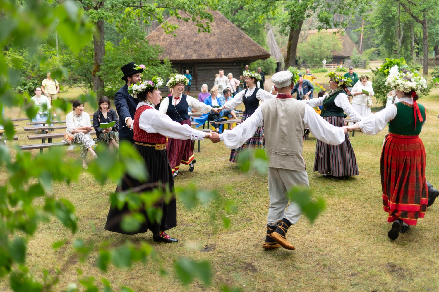 Cilvēki tautastērpos un krāšņos Jāņu vainagos iet tradicionālās rotaļās.