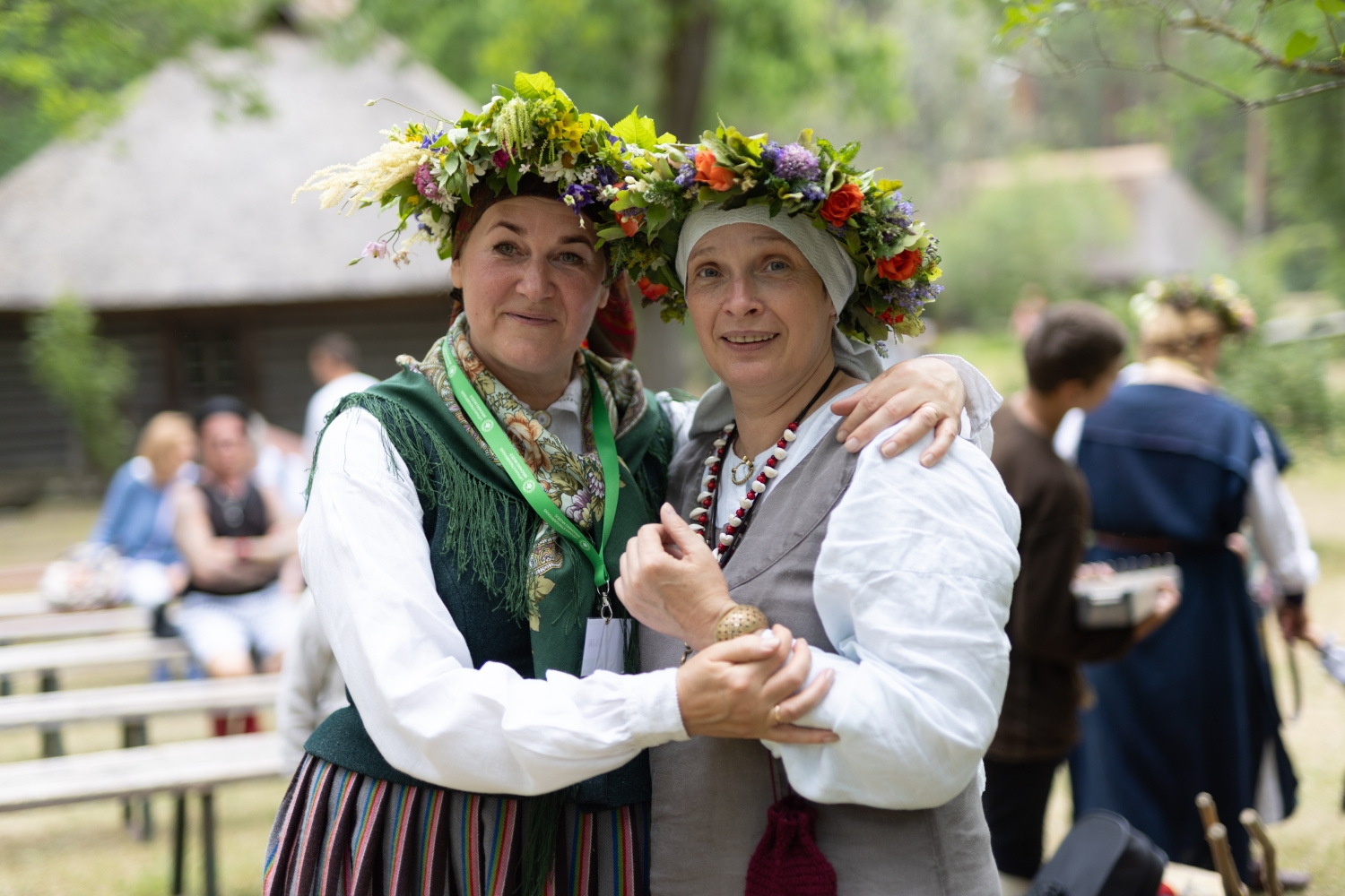 Divas sievietes tautastērpos ar košiem ziedu vainagiem galvā