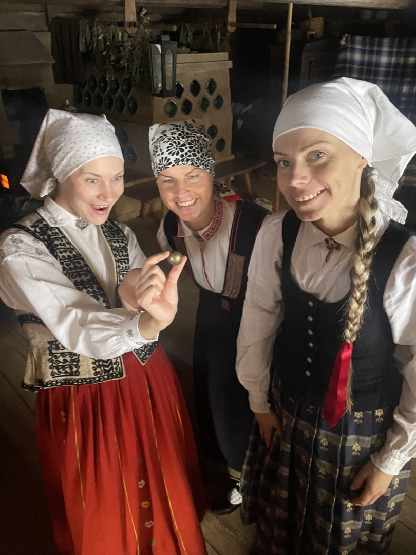 Trīs meitenes tautastērpos priecājas par atrastu Meteņu zelta pogu.