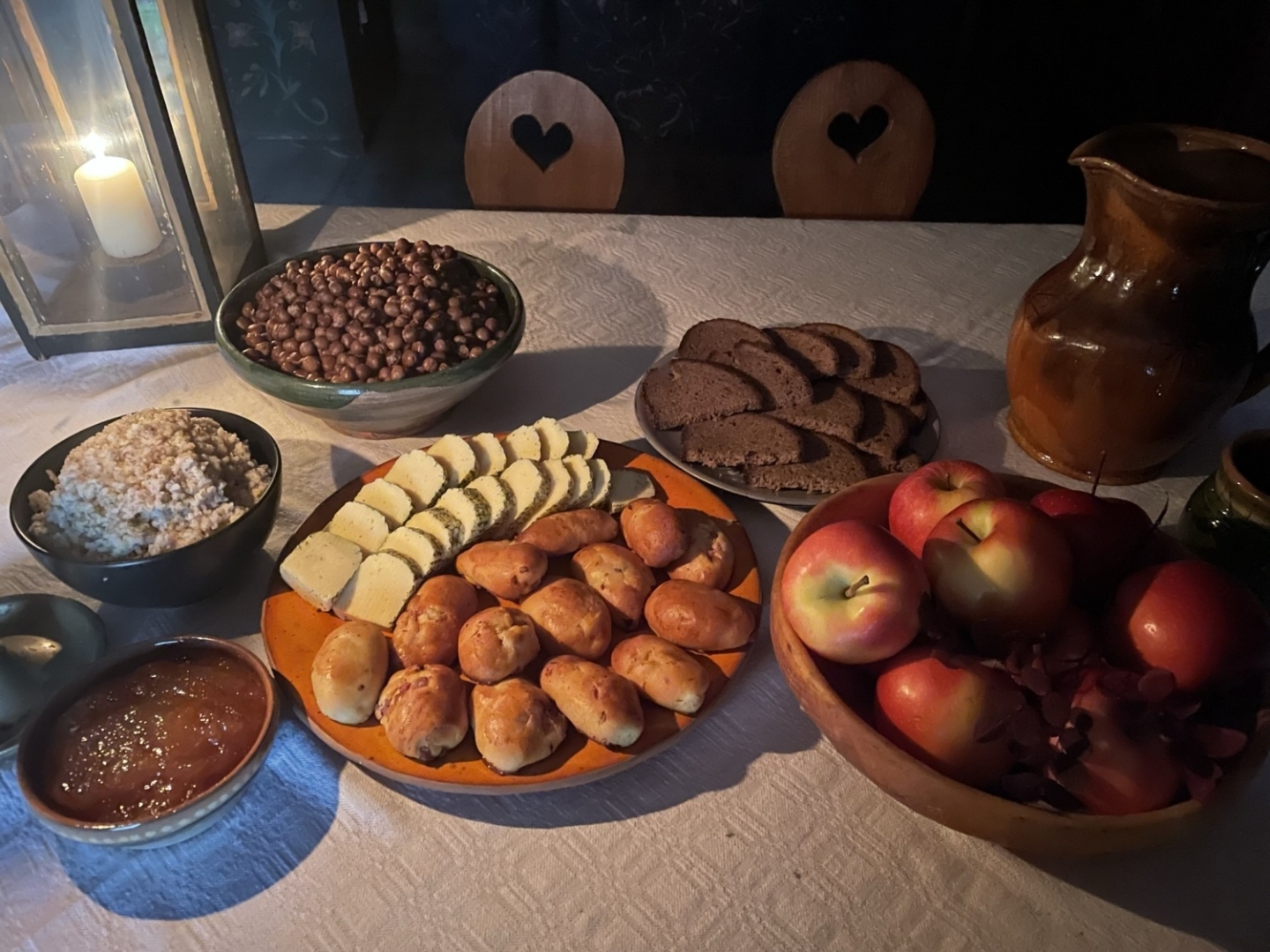 Tradicionālais veļu mielasts māla un koka traukos uz koka galda: tuvplānā redzami pīrāgi, biezputra, pelēkie zirņi, āboli, rupjmaize un siers Latvijas Etnogrāfiskā brīvdabas muzeja klētī.