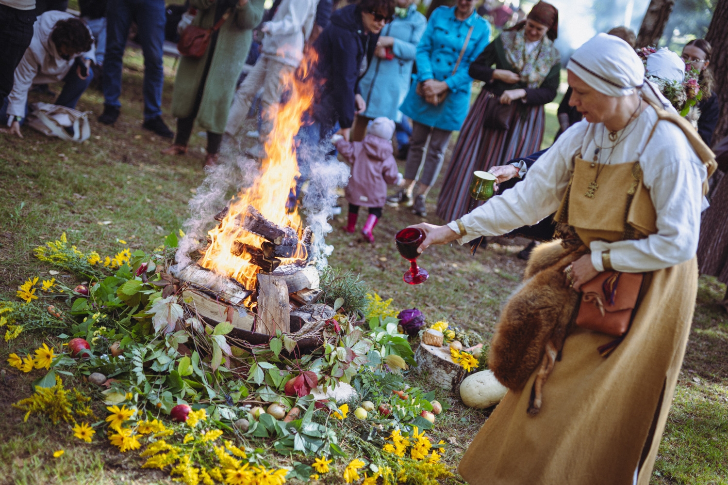Rituālais ugunskurs; sieviete ziedo ugunij maizes kukulīti ražas svētku rituālā