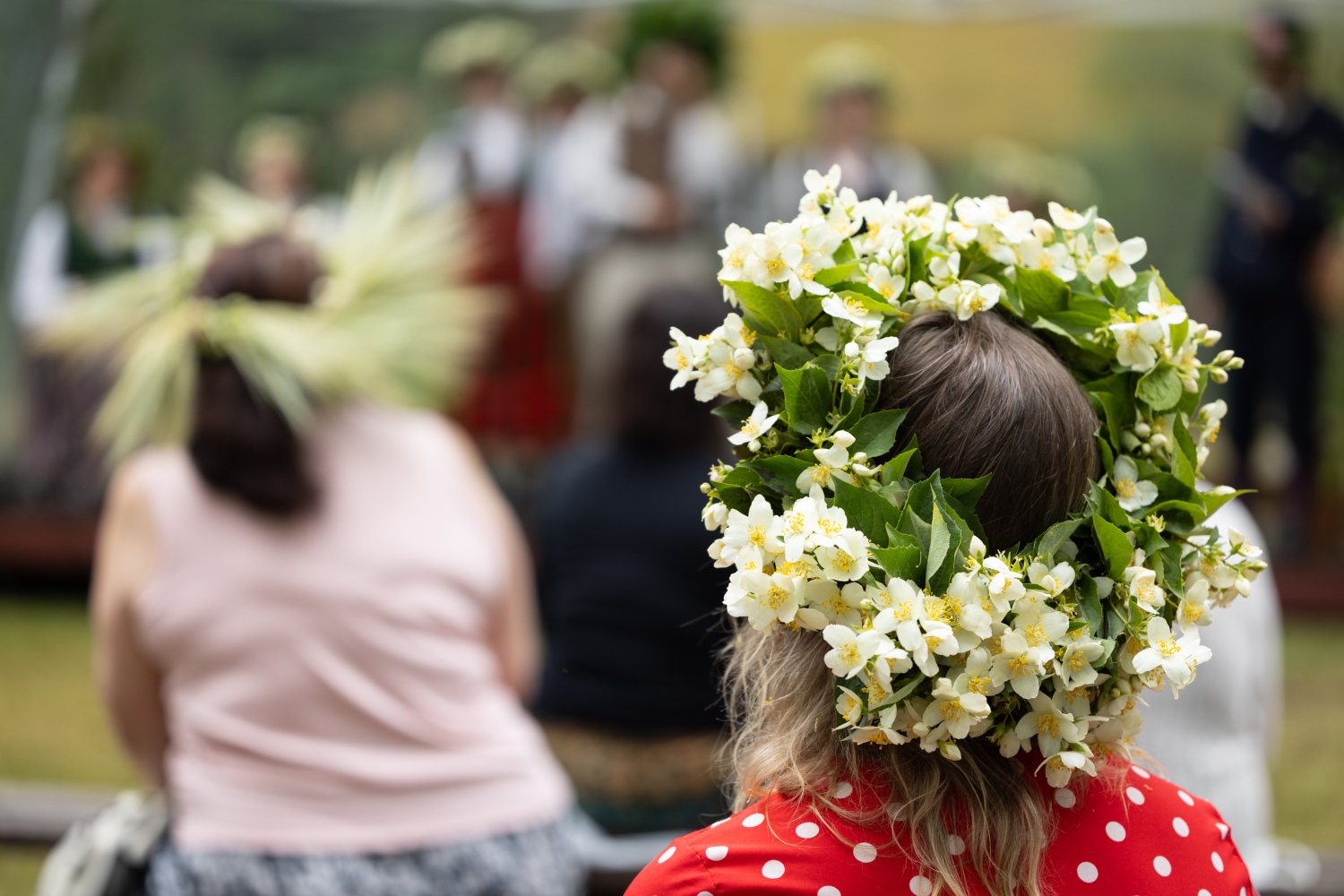 Skats no mugurpuses: meitene ar krāšņu un kuplu balto jasmīnziedu vainagu galvā