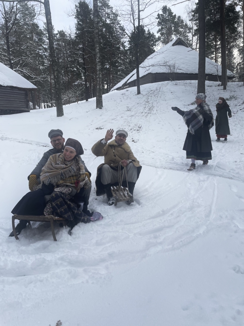 Jaunieši ziemīgā, sniegotā ainavā laižas lejā no kalna ar ragaviņām.
