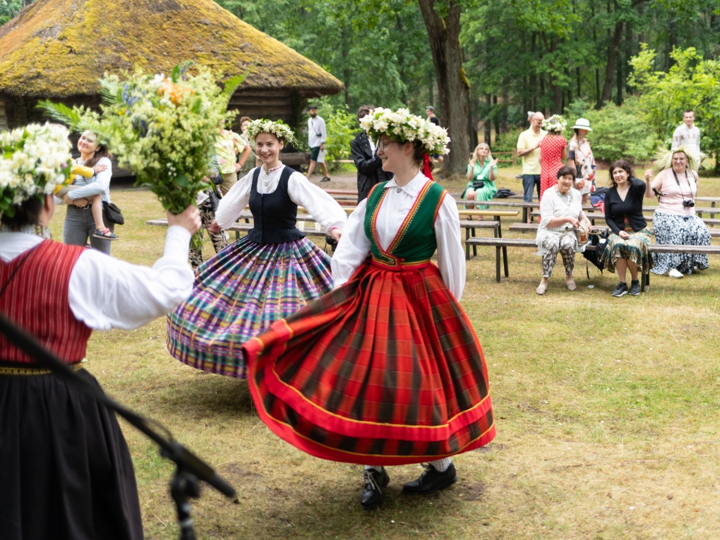 Meitenes latviešu tautastērpos un puķu vainagos dejo Jāņu danci