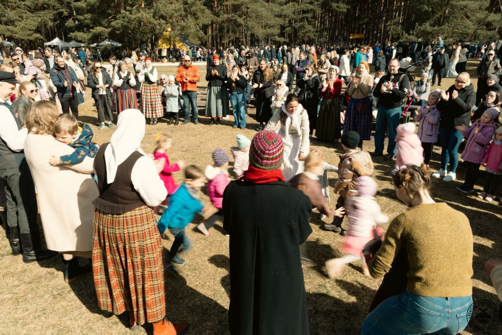 Lieldienu svinību dalībnieki kopā iet tradicionālajās latviešu tautas rotaļās.
