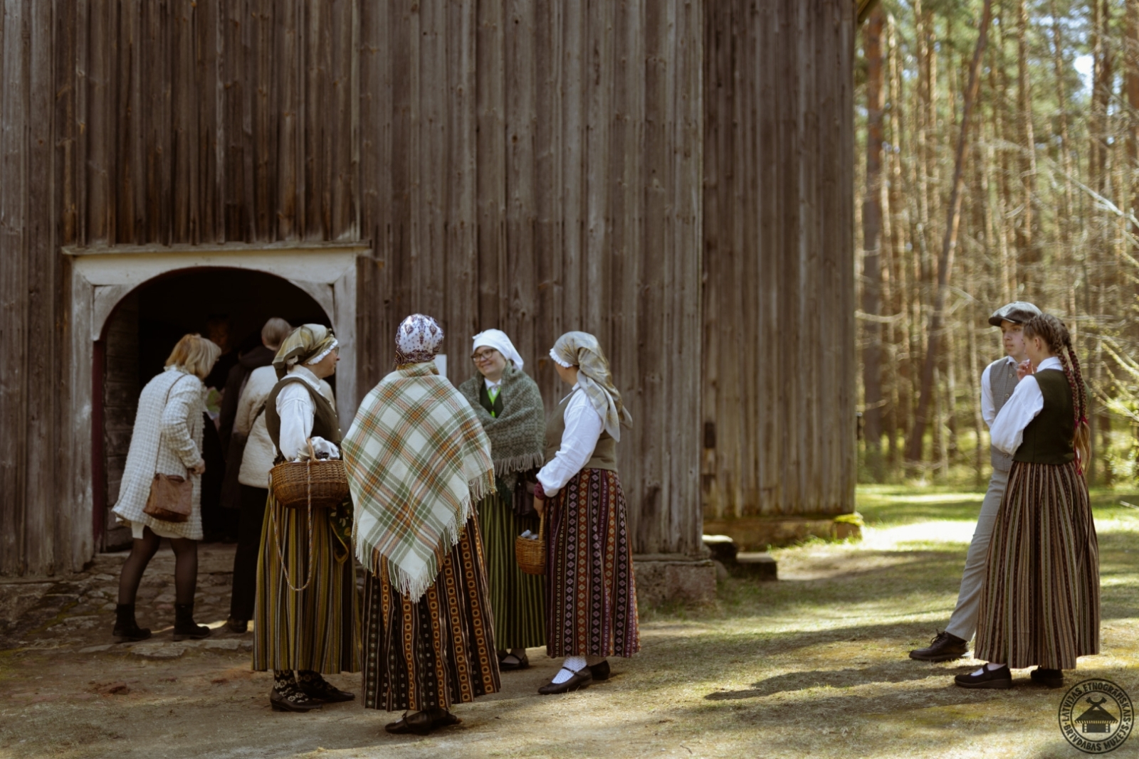 Sievietes krāšņos tautastērpos sapulcējušās pie vēsturiskās Bornes baznīcas koka durvīm.