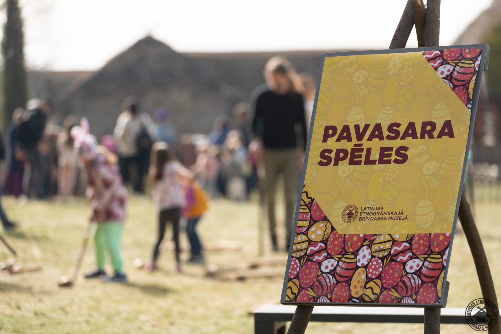 Plakāts: Pavasara spēles - fonā bērni aktīvi piedalās brīvdabas aktivitātēs