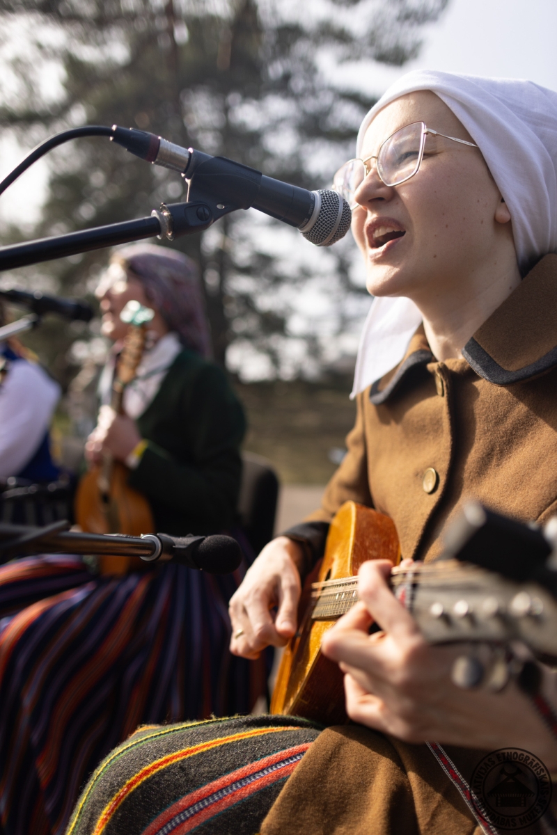 Folkloras kopas dalībniece spēlē mandolīnu un dzied svētku dziesmas.