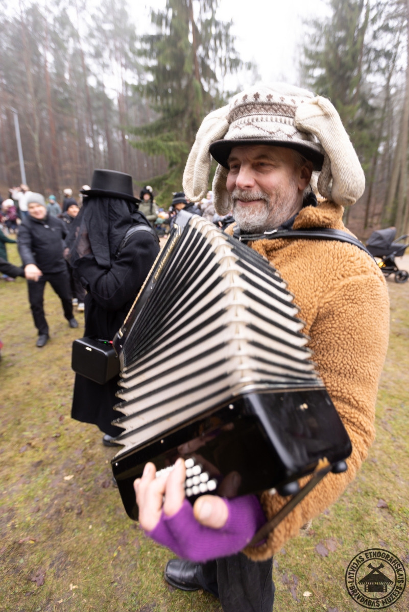 Masku gājiena dalībnieki dzied un spēlē tamburīnu. 