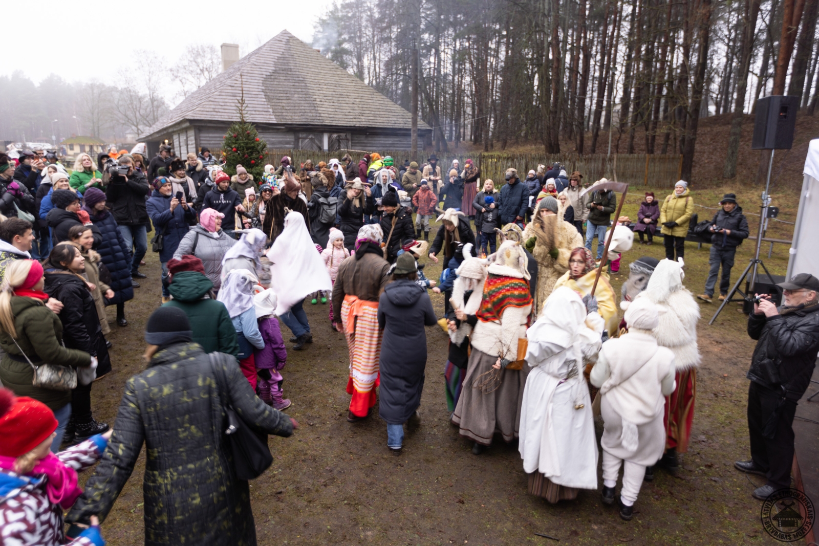 Masku gājiena dalībnieki velk bluķi cauri muzeja ciemam. 