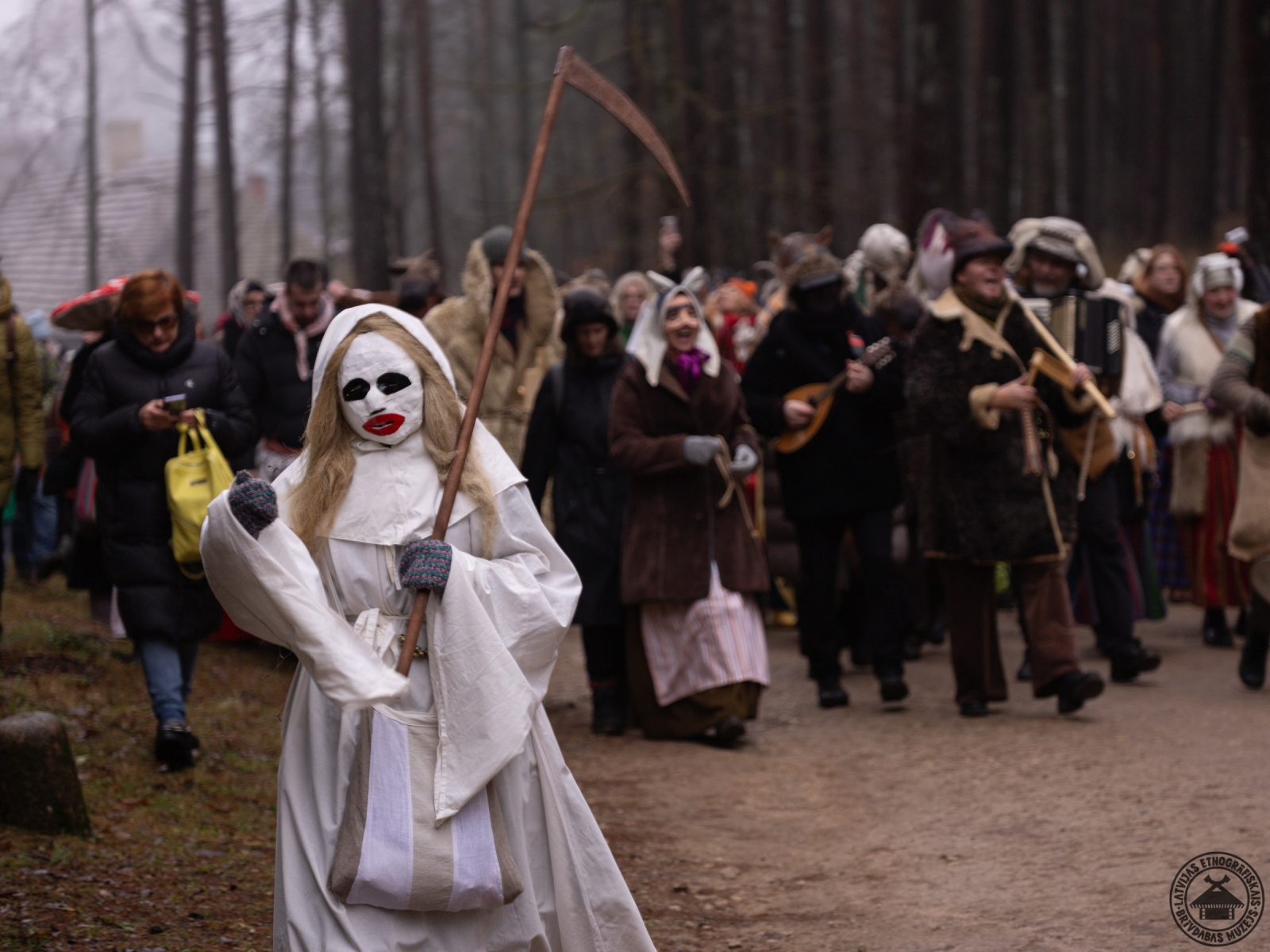 Masku gājiens Ziemassvētkos; priekšplānā dalībnieks tradicionālajā Nāves maskā. 