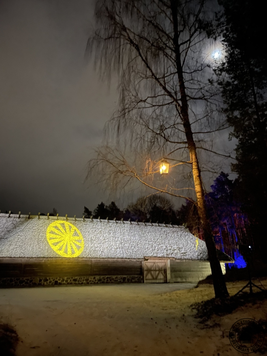 Kurzemes laidars tumsā ar dzeltena rata (saules simbola) gaismas projekciju uz sienas. 
