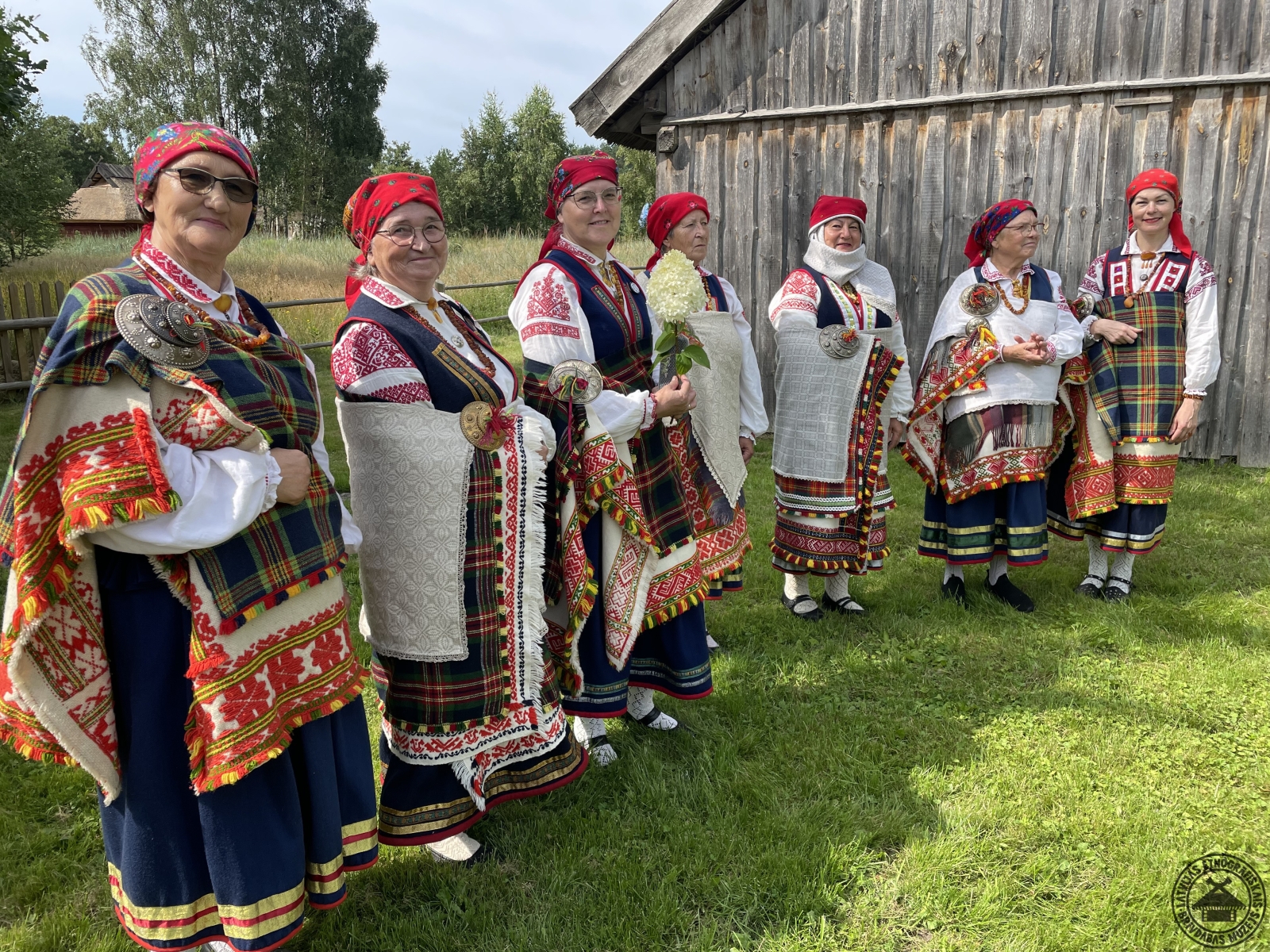 Vītolnieku sētas pagalmā svinīgi sastājušās sievas krāšņos un autentiskos Rucavas tautastērpos. 