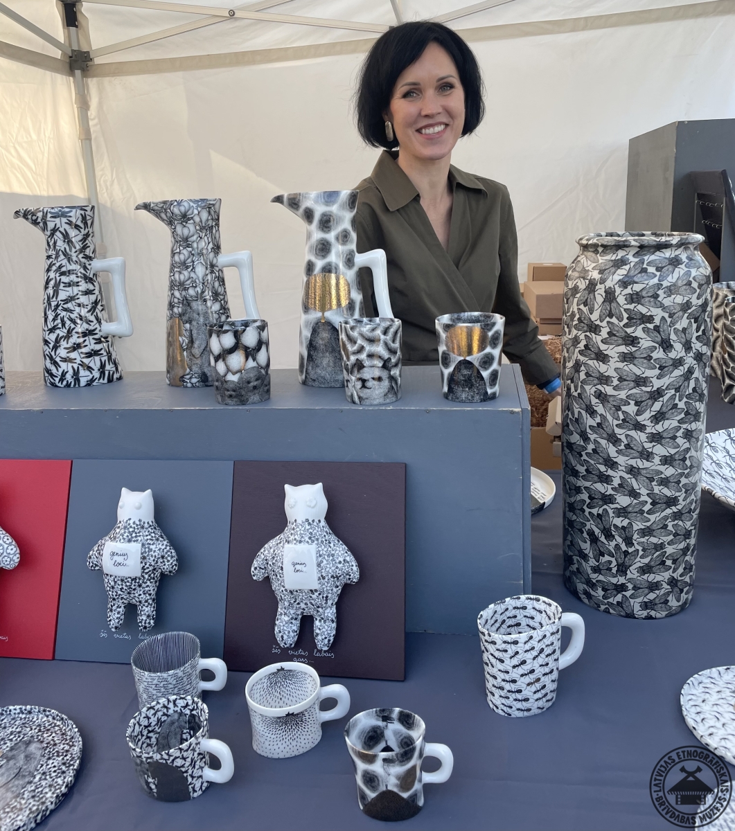 Māksliniece savā stendā starp apgleznotiem porcelāna darbiem – vāzēm, krūzēm un šķīvjiem. 