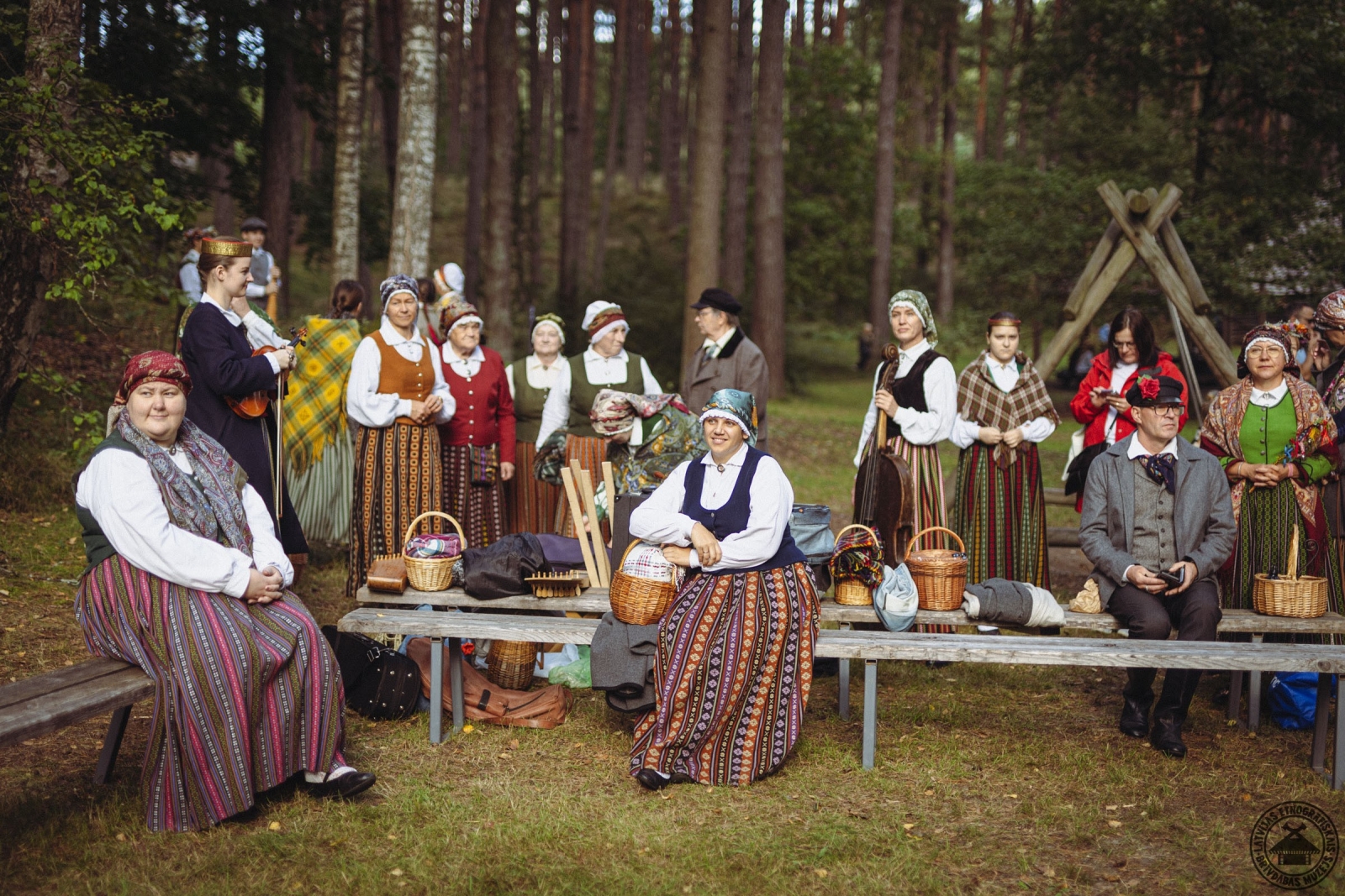 Folkloras kopa pilnos tautastērpos pozē kopbildei muzeja vidē. 