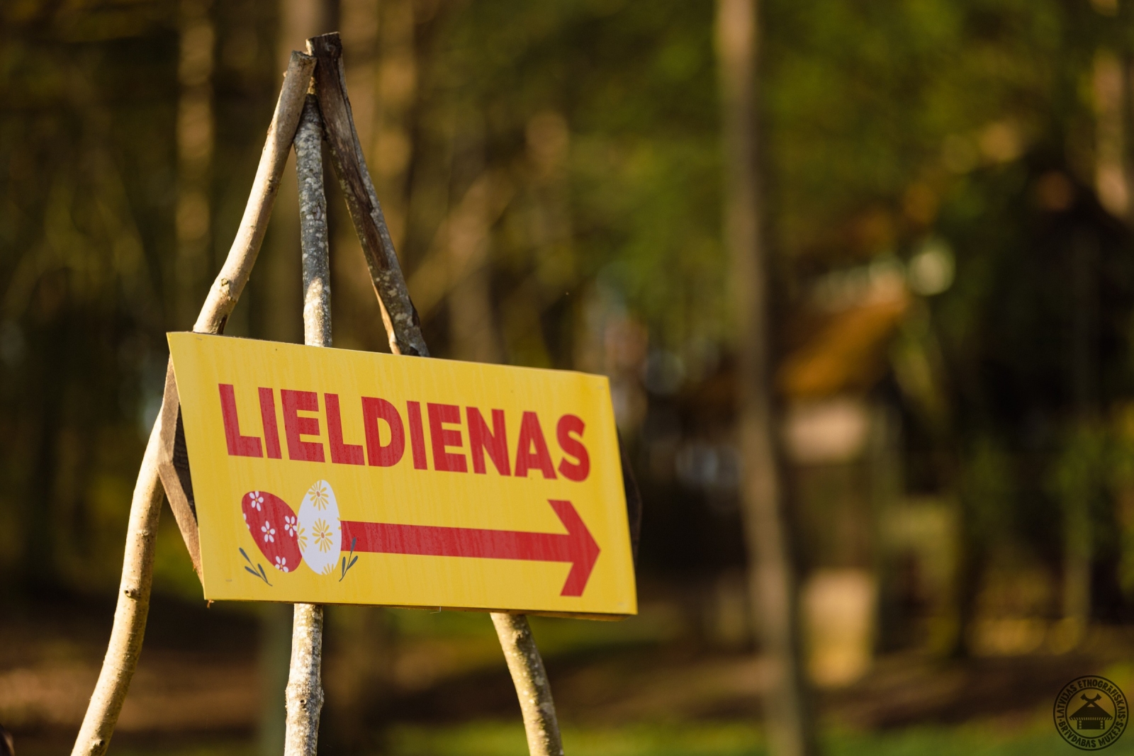 Koka norāde ar uzrakstu Lieldienas, kas rāda virzienu uz pasākuma norises vietu. 