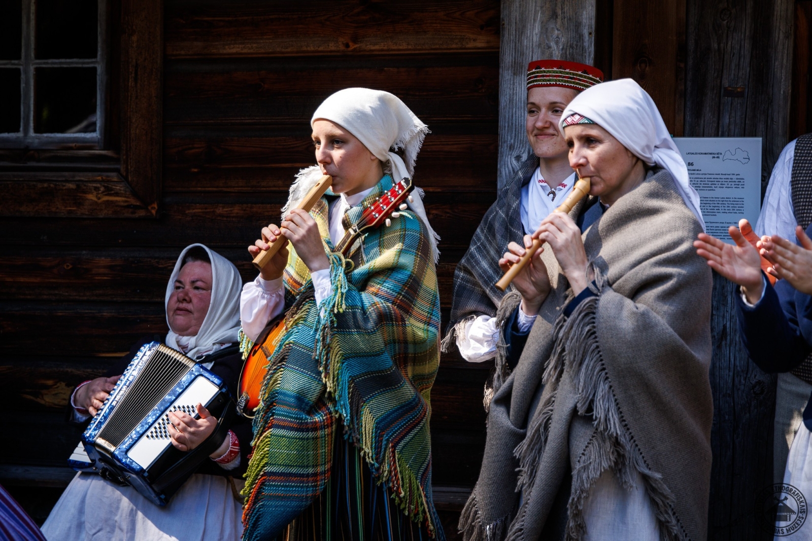Divas sievietes tautastērpos spēlē stabules, trešā pavada uz akordeona. 