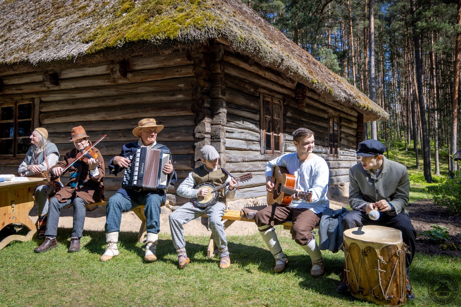Mūziķu kopa uz koka sola spēlē dažādus tradicionālos mūzikas instrumentus. 