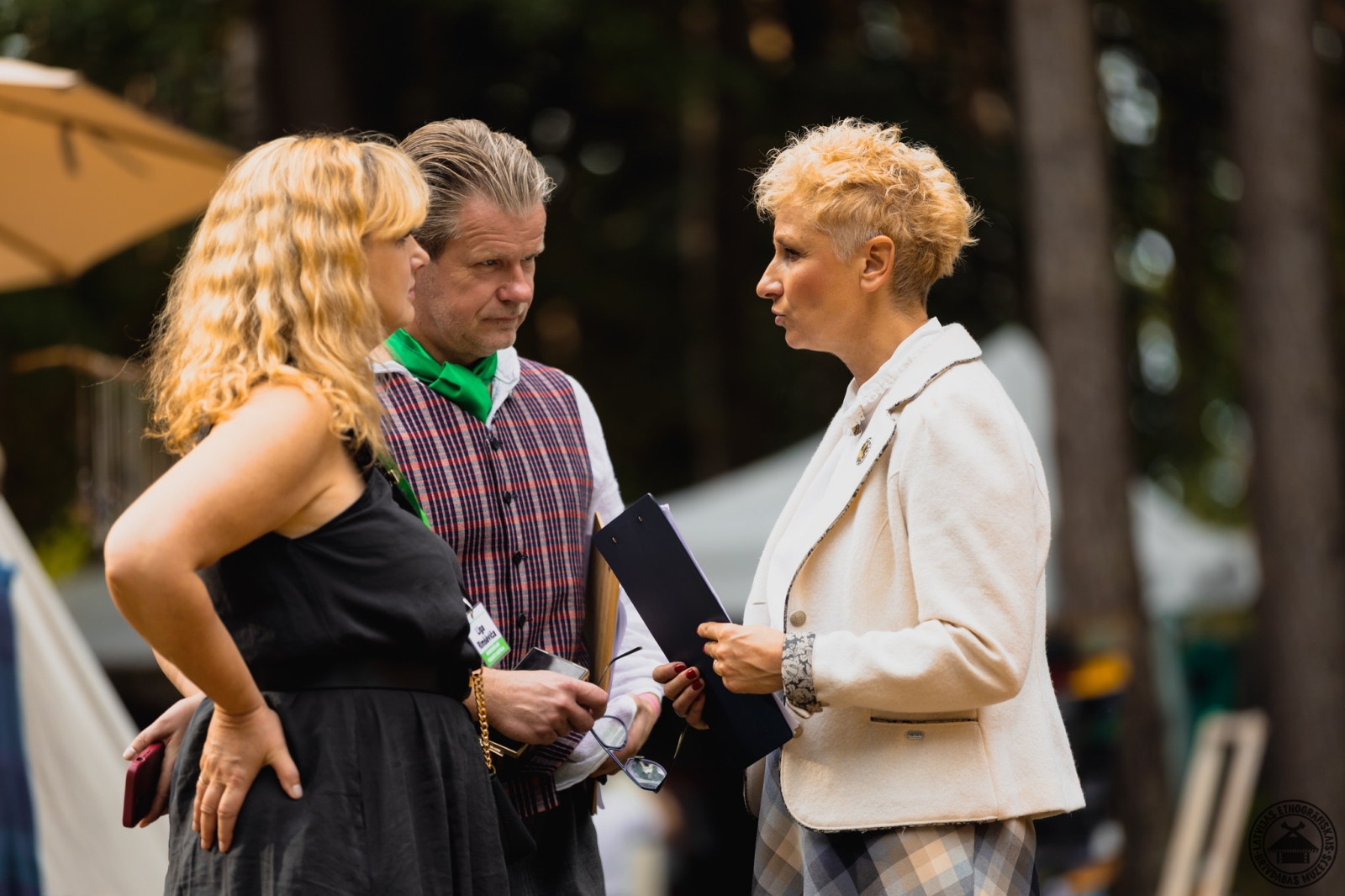 Trīs cilvēku saruna; starp viņiem tirgus kultūras programmas vadītāja. 