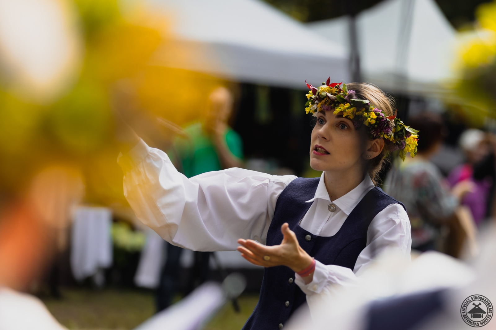 Portrets: meitene tautastērpā ar krāšņu ziedu vainagu galvā. 