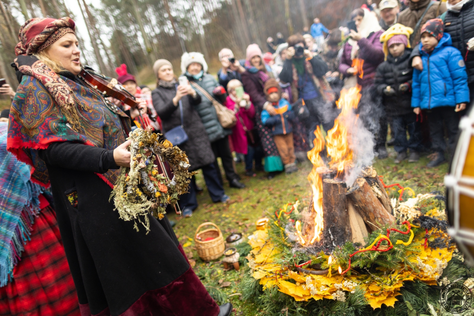 Sieviete tautastērpā pie ugunskura, piedaloties rituāla norisē. 