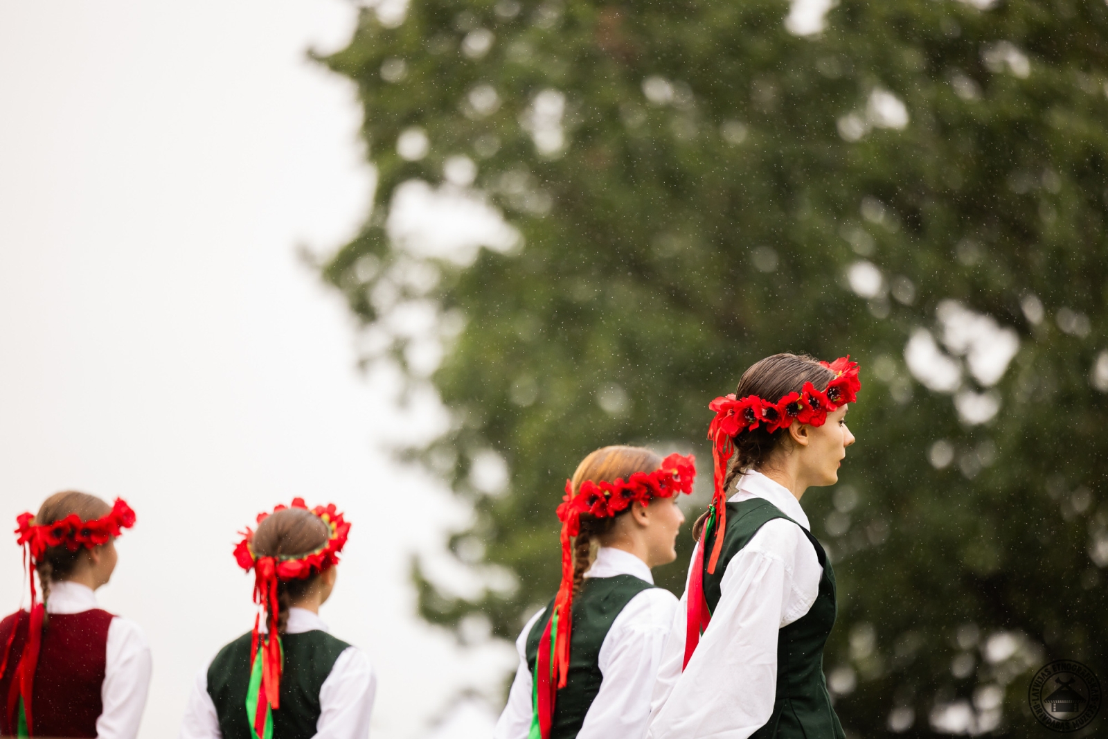 Dejotājas tautastērpos ar koši sarkaniem ziedu vainagiem galvā. 