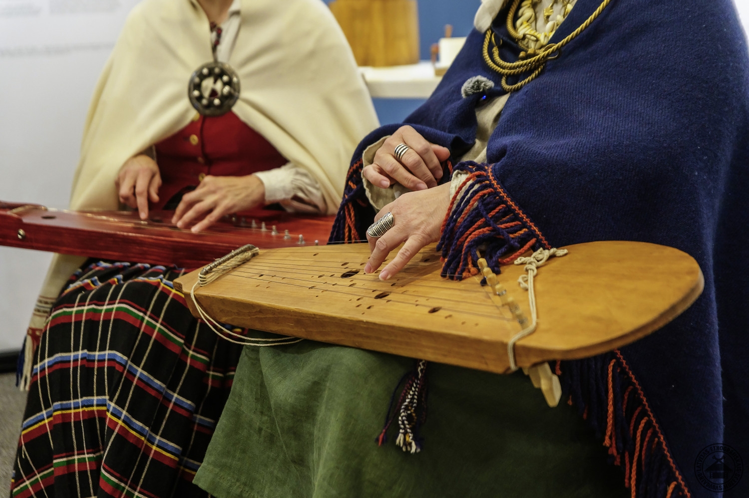 Muzikāls priekšnesums: divas sievietes tautastērpos spēlē kokles. 