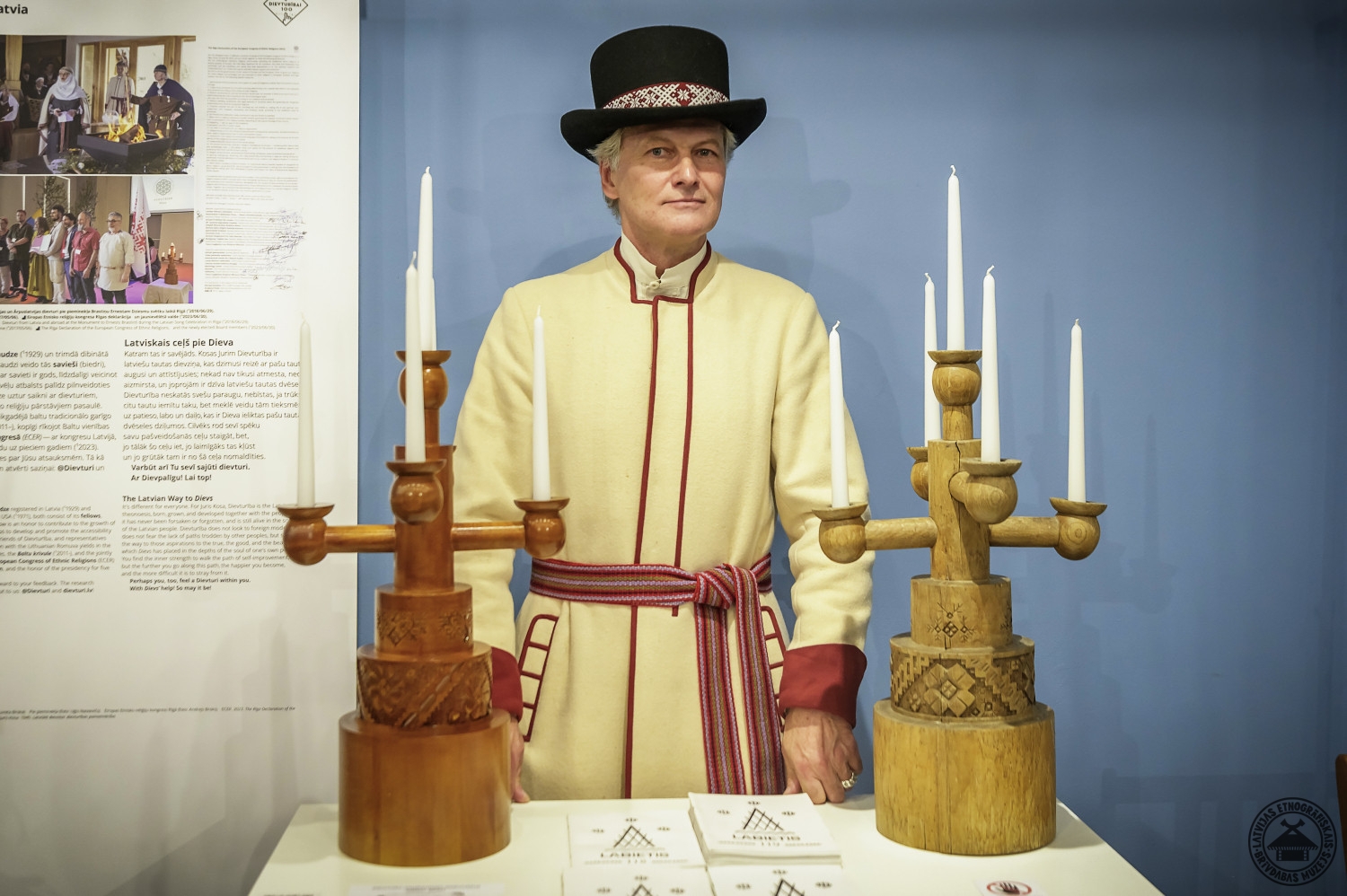 Dievturu vadītājs ar diviem tradicionāliem koka svečturiem rokās. 