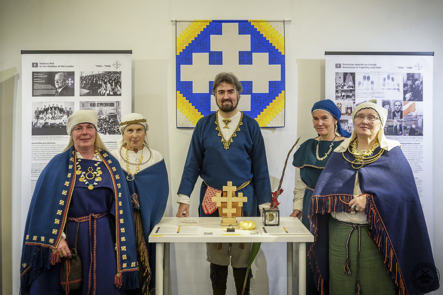 Dievturu krusta zīme un pieci cilvēki tautastērpos izstādes atklāšanā. 