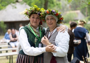 Divas sievietes tautastērpos ar košiem ziedu vainagiem galvā