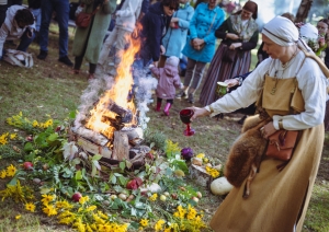 Rituālais ugunskurs; sieviete ziedo ugunij maizes kukulīti ražas svētku rituālā