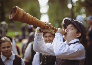 Zēns tautastērpā pūš pašdarinātu raga tauri, mācoties senās tradīcijas.