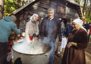 Dalībnieki stāv ap lielu, kūpošu rudens zupas katlu brīvā dabā